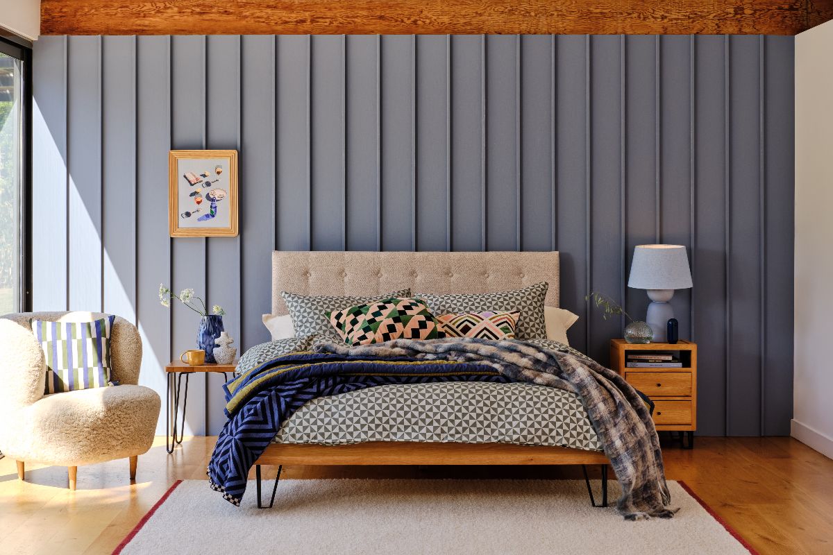 A modern bathroom with 3D wallcoverings painted in blue, wood furniture, a boucle armchair in a corner and a central bed.