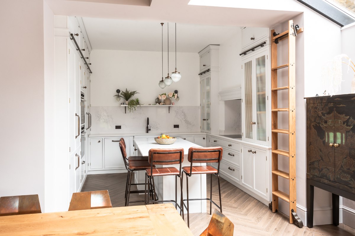 White kitchen design with fluted glass cabinets, a central island, and a wood ladder.