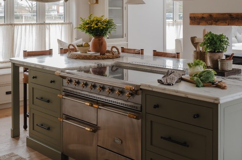 A calm cooking space with a central unit painted in dark green with preparation space, integrated seating, and a statement range cooker.