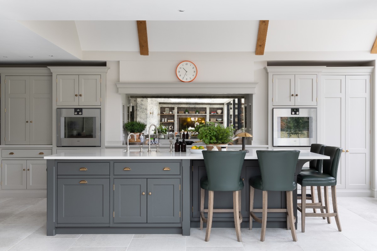 A classic design with off-white and dark grey cabinetry, a central island with seating, and a mirrored splashback above the cooking zone.