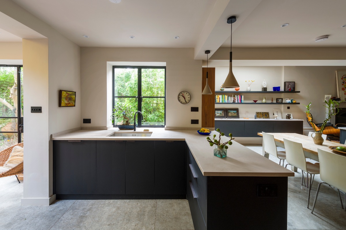 L-shaped cabinetry with dark units, concrete-effect worktops, an inset sink, black tap, and steel-framed glazing.