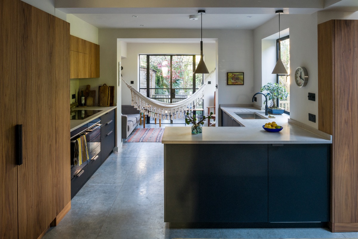 Mid-century modern kitchen with walnut and black veneer cabinetry, dark handles, concrete-effect worktops and an adjoining snug.
