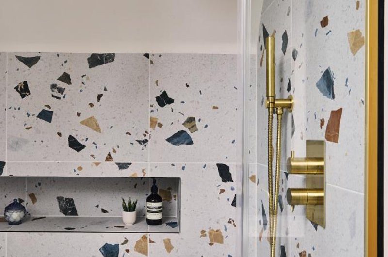 A shower zone with terrazzo tiles, a storage niche, and gold shower system.