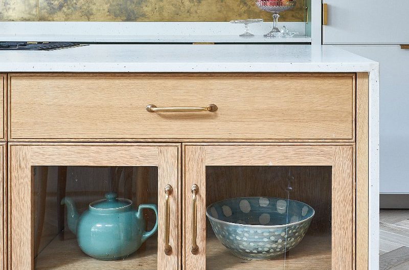 Closeup at a kitchen island display cabinet with wood, glass fronts and brass handles.
