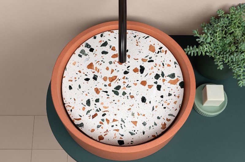 A closeup at a terrazzo basin with a sleek green countertop and black brassware.