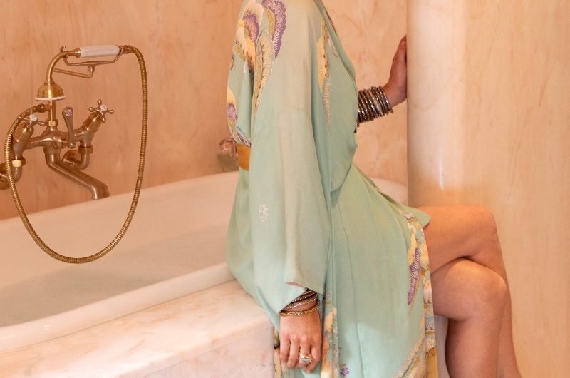 Kate Moss posing on her fitted bath adorned with marble and featuring classic brassware in the background.