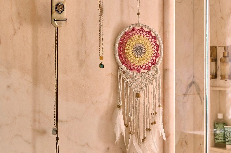 Closeup at brushed brass wall hooks on a pink marble wall.