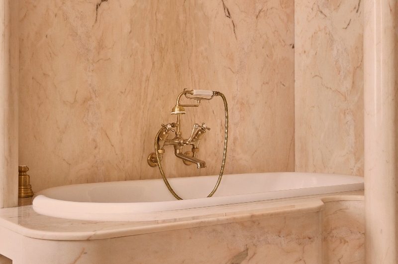 Kate Moss' bathroom features a fitted bath, clad in pink marble with pink marble wall cladding, gold brassware, and vintage gold wall lights.