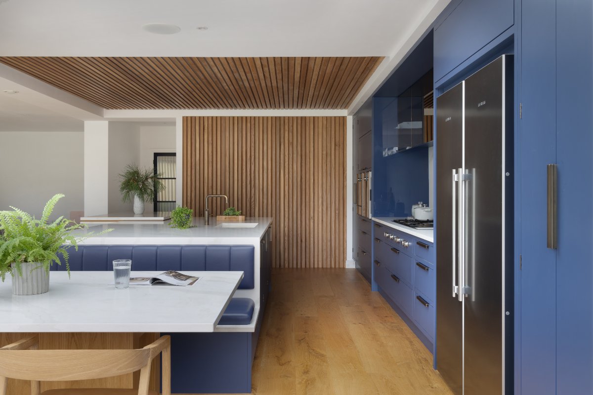 One wall cabinetry painted in a vibrant blue with an island with booth seating, sink and tap, and panelled ceiling and wall.