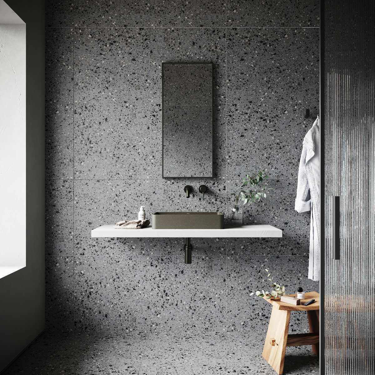 A contemporary bathroom design with a wall-mounted countertop, olive green basin, grey terrazzo wall and floor tiles, and black accessories.