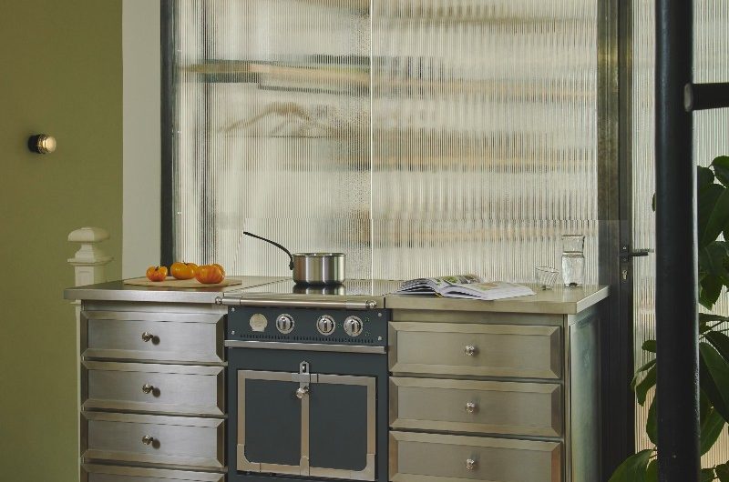 A stainless steel unit with a built-in range cooker painted in blue which has an induction hob, with an industrial pendant above it.