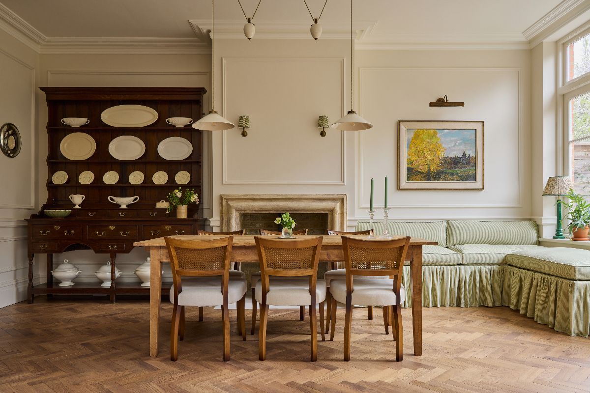 Elegant dining room with Boiserie wallcoverings, a vintage dresser, a wood table and chairs, and a banquette area upholstered in green ruffled fabric.