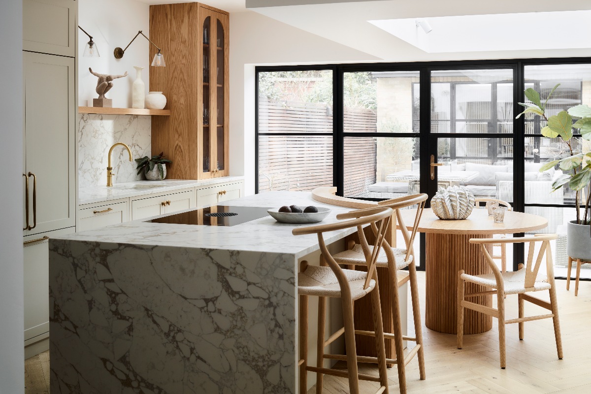 Neutral kitchen design with a central island with a waterfall worktop edge, seating, and built-in hob, with a run of cabinetry behind it.