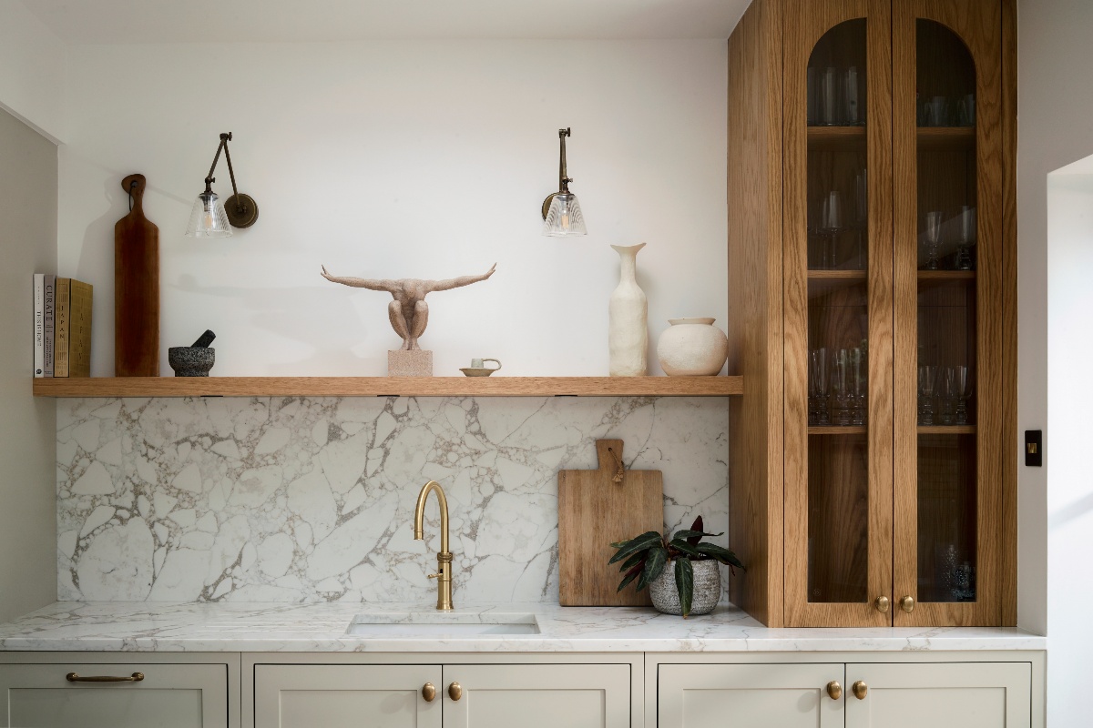 A neutral cabinetry run offering storage, space for a sink area, marbled surfaces, an open shelf for displaying decor, and an oak cabinet with glass doors.