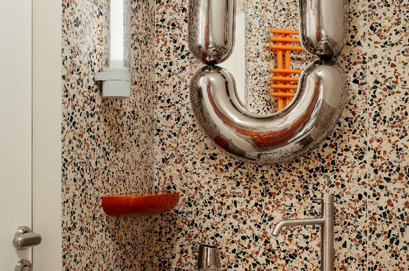 Terrazzo-drenched cloakroom with a quirky mirror, orange radiator, and red soap holder.