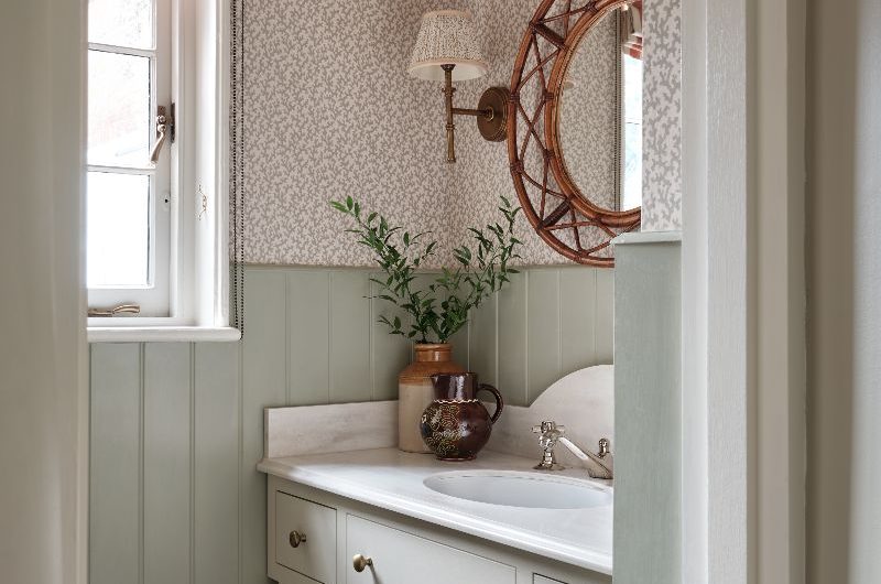 Classic bathroom design with floral wallpaper, sage green tongue and groove wall panels, a timeless vanity with drawers and open storage, marble countertop and inset sink.