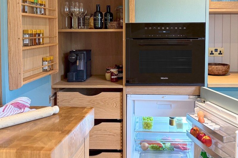A sleek blue and wood kitchen with small built-in appliances and a pantry.