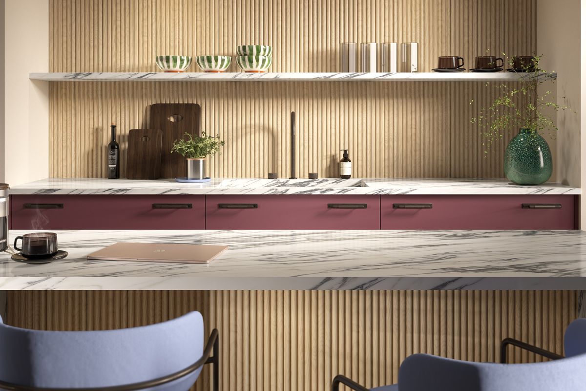 Modern kitchen design with fluted wall panelling, a peninsula with matching panelling on its base and marble countertop, and a run of burgundy cabinetry in the background with a stone shelf.
