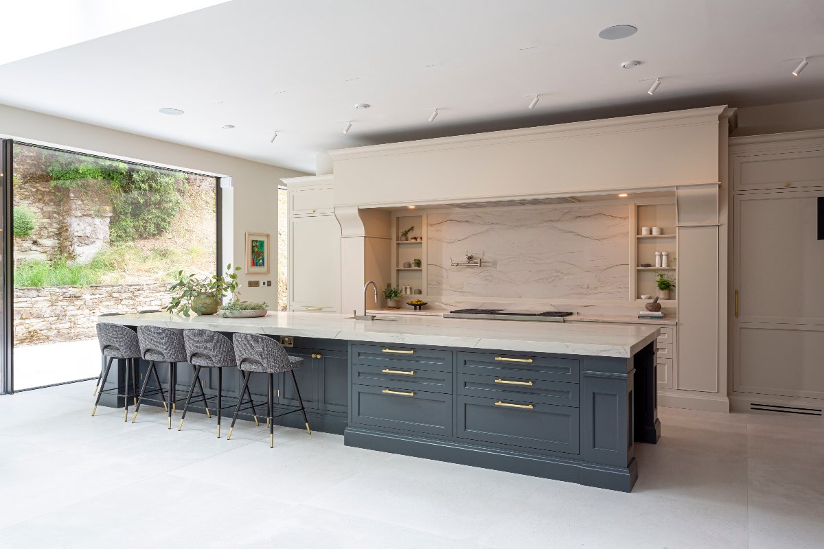 Neutral cabinetry with slim frames, a cooking zone with a single slab splashback, pot filler tap, open shelving, and a range cooker, with a large island with storage, sink and tap, preparation space, and seating.