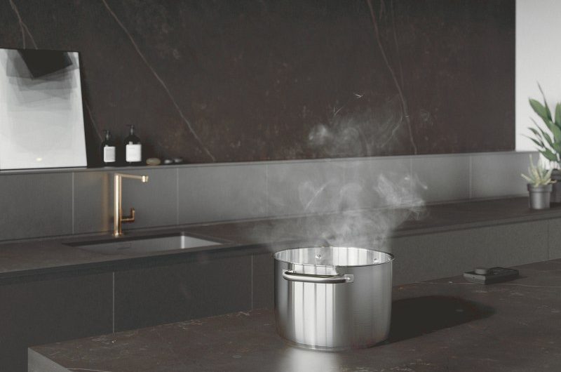 A dark, industrial-style kitchen design with handleless cabinets and veiny porcelain surfaces. The matching island includes invisible induction with a ceiling-mounted extractor.