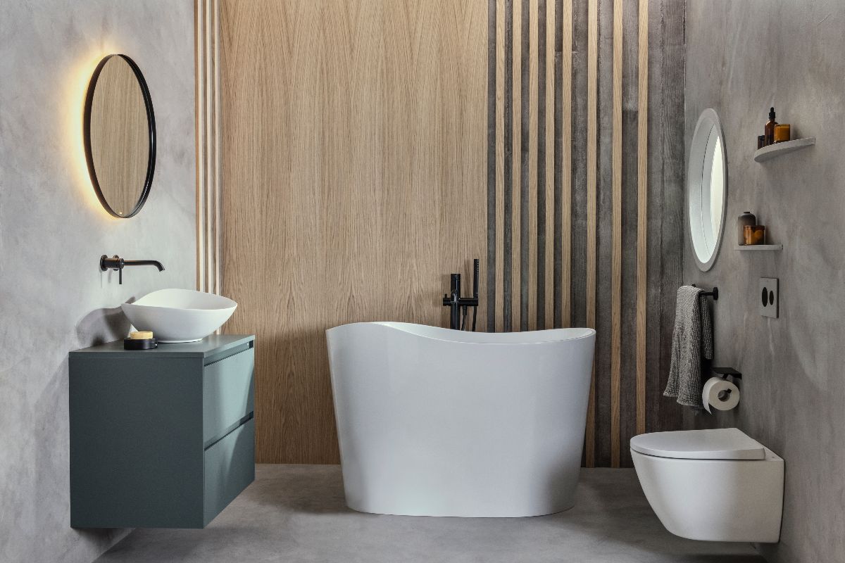 A calming bathroom design with a sculptural tub, wall-mounted WC and green vanity unit, with concrete-effect surfaces on the wall and floor and wood panelling. 