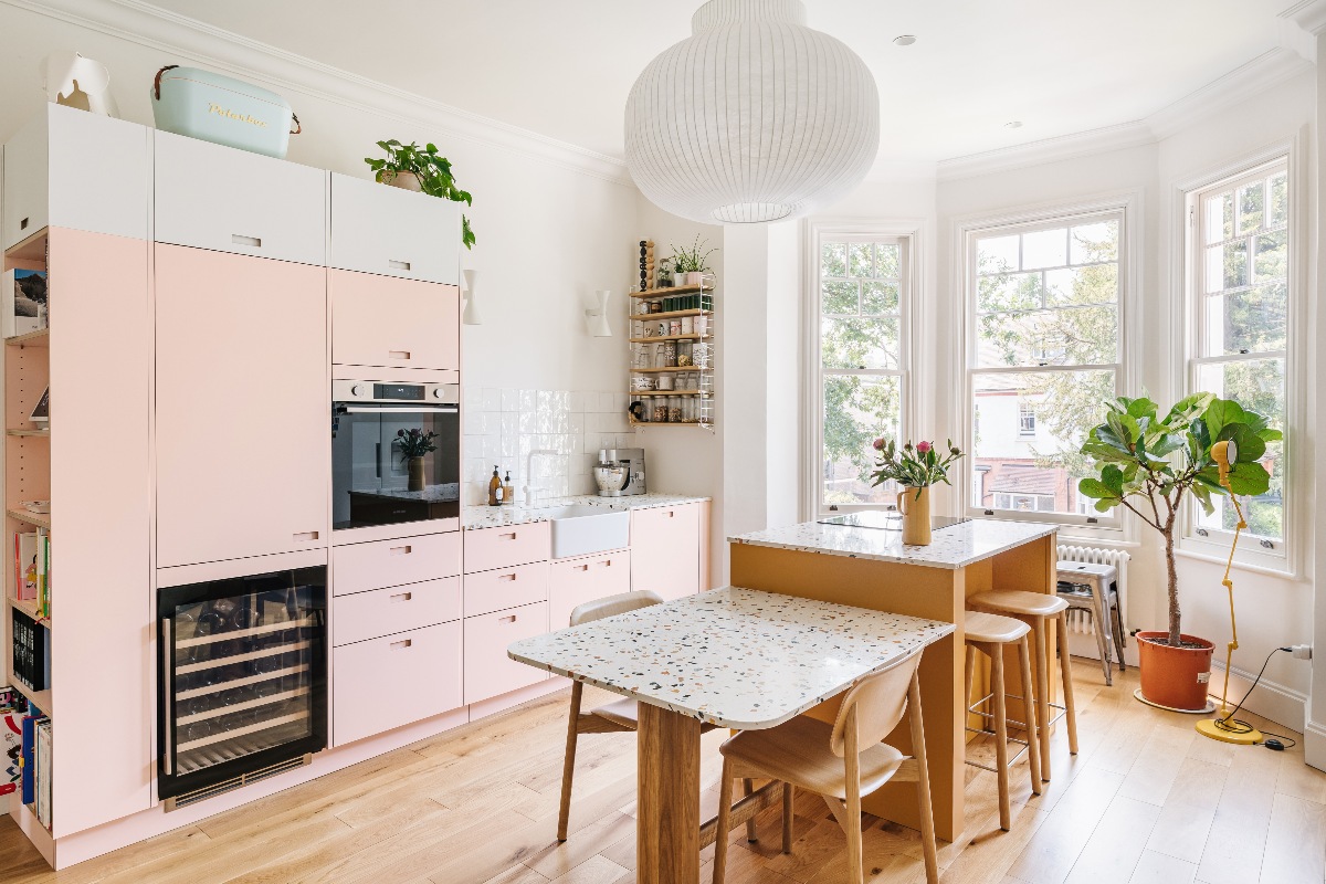 A single run of pink cabinetry, terrazzo surfaces, a wood split level island and table, and wood flooring.