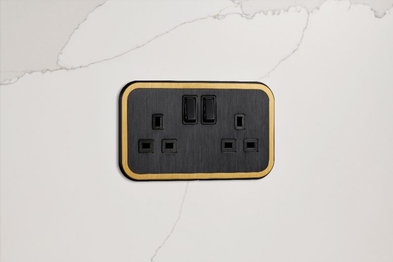Black and gold power socket on a veiny splashback.