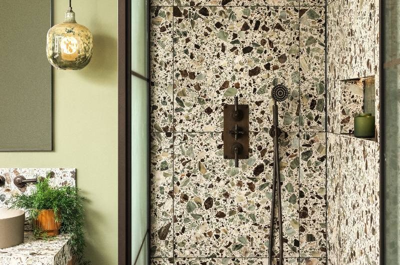 A shower dressed in terrazzo surfaces with black brassware, storage niche, and steel-framed panel.