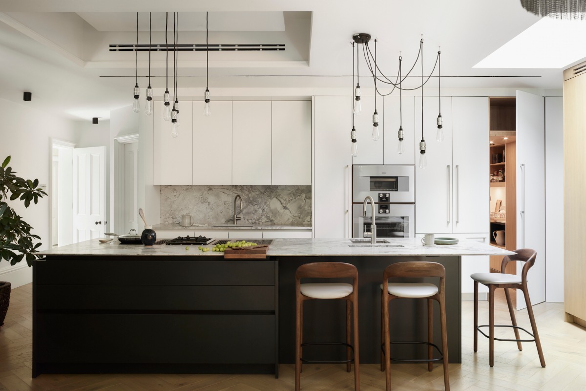 A handleless island with a matt lacquer finish, breakfast bar, built-in cooktop appliances with integrated ventilation, and a preparation sink in a luxury kitchen.