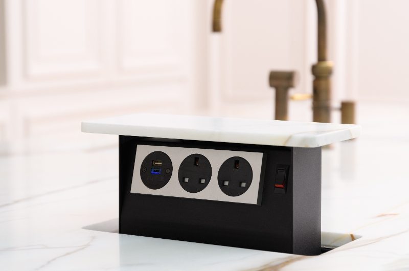 A kitchen island with marble surfaces and a pop-up socket.