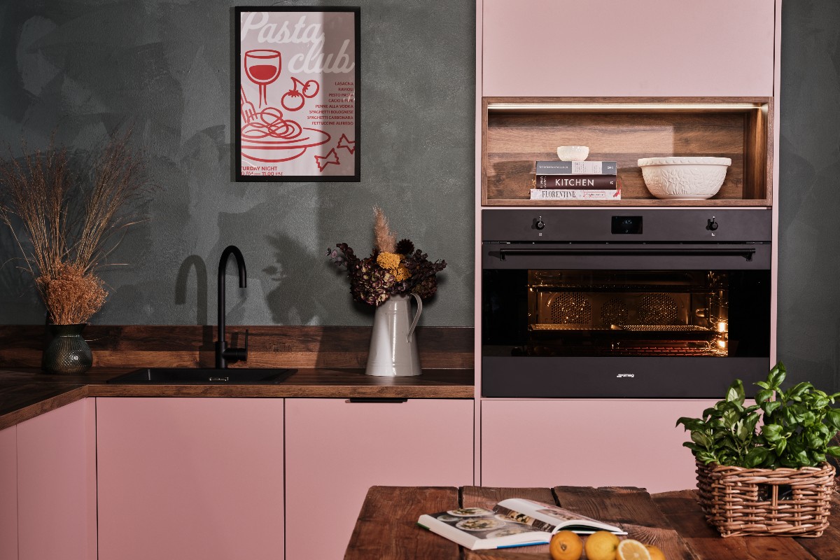 A pink kitchen with wood work surfaces, dark grey walls, a built-in oven and central island.