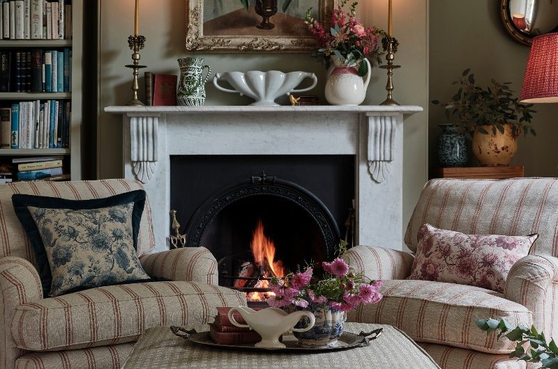A living room design with striped armchairs, patterned ottoman, and a fireplace.