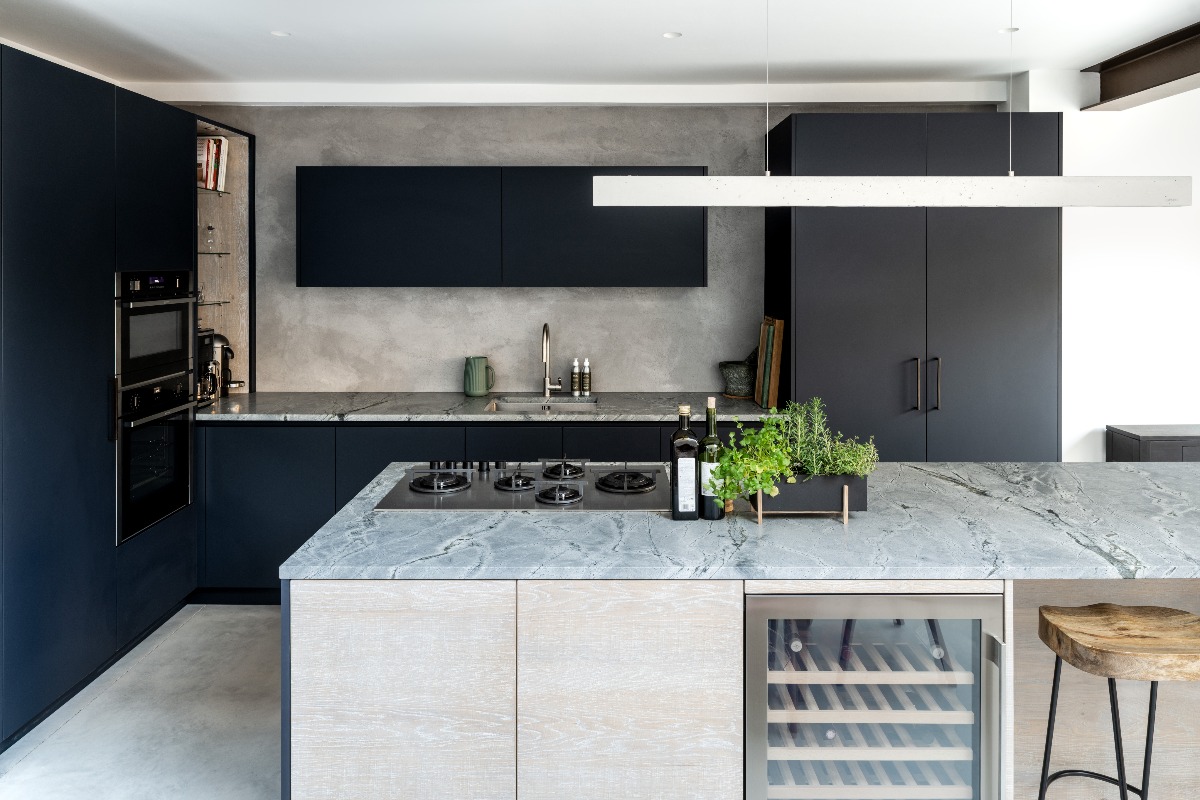 A kitchen island design with a gas hob, built-in wine fridge, and breakfast bar seating, with oak-fronted cabinetry topped with a sintered stone worktop and a run of white cabinetry behind it
