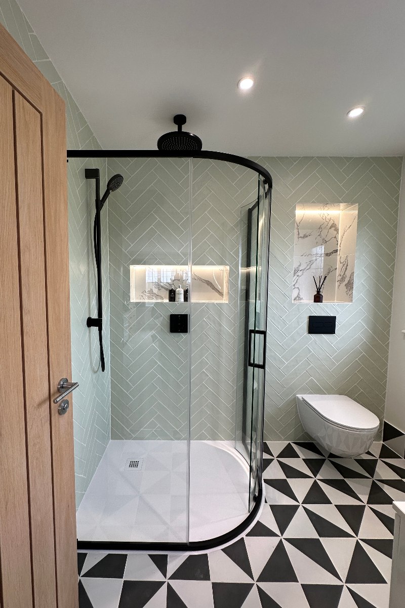A green bathroom with herringbone wall tiles, black and white flooring, white sanitaryware and a shower zone with a curved enclosure.