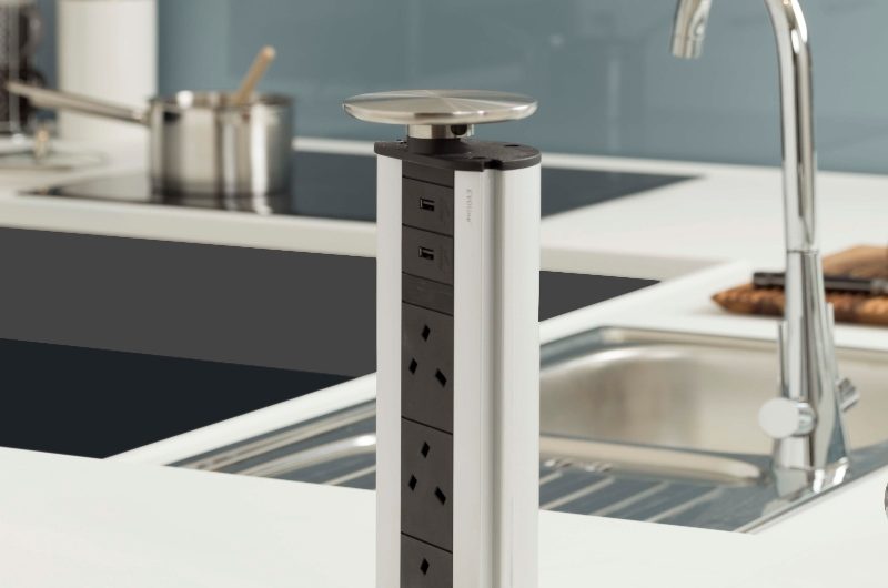 A modern kitchen with white surfaces, a chrome sink and tap, and a pop-up power plug.