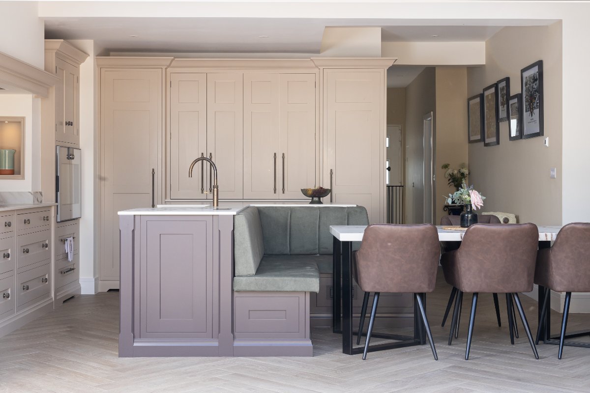 A pale pink kitchen design with a multi-functional island painted in a darker purple with seating and a dining table.