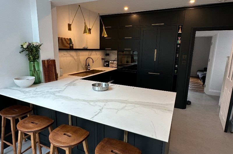 A classic kitchen design with dark cabinetry and veiny surfaces, with an invisible hob built within the peninsula worktop and a matching invisibile ceiling extractor.