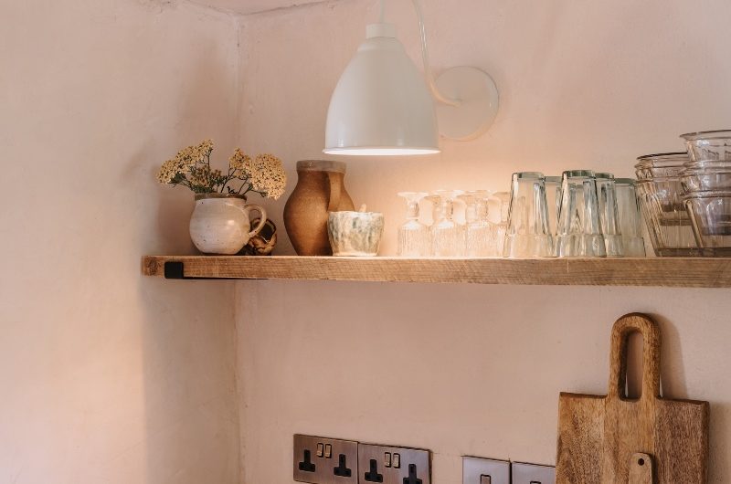 A rustic kitchen with textures walls, wood worktops, nickel power sockets and a wood shelf.
