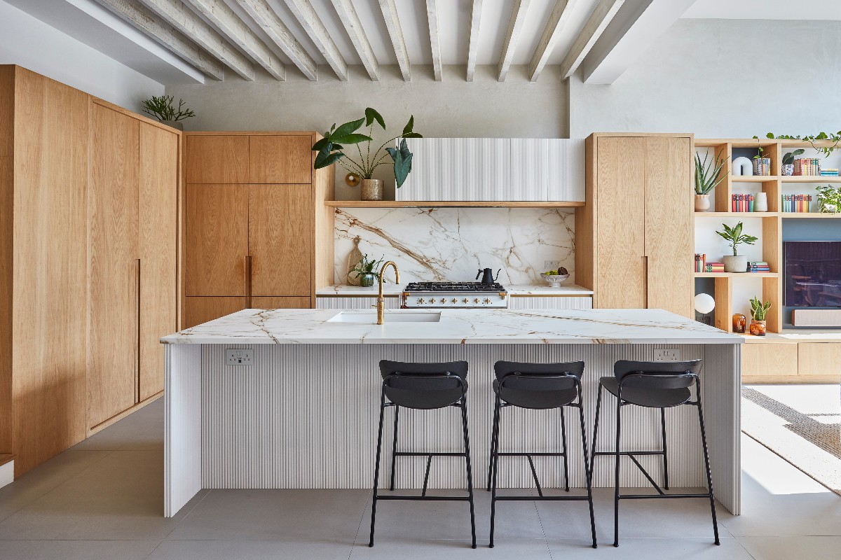 Wood kitchen design with statement marble surfaces and a central island with white power sockets.