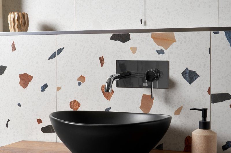 Vanity area with a wood countertop, black basin, chrome brassware, large-format tiles, and a blue circular mirror.