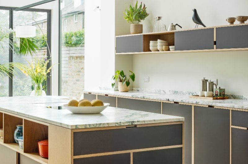 A central unit made from wood with closed and open storage, and a run of cabinets with stone surfaces.