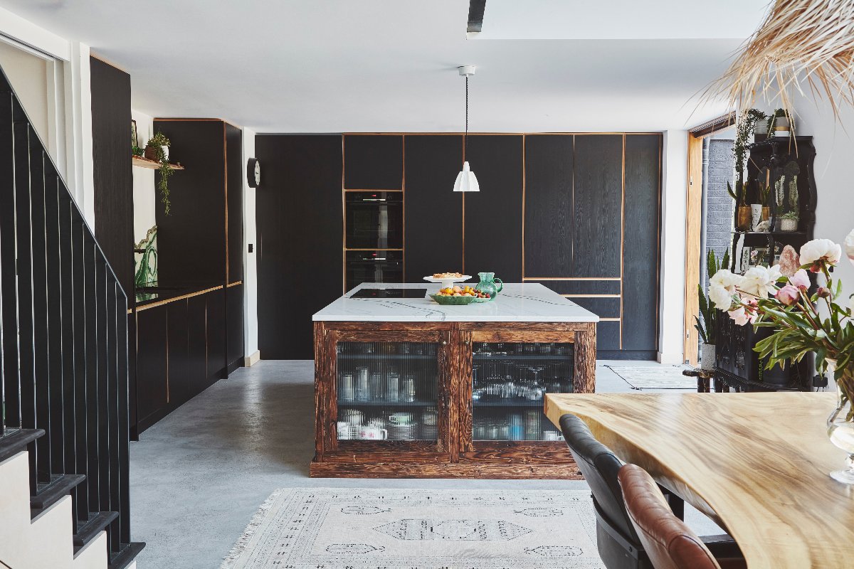 A dark kitchen with floor-to-ceiling handleless cabinetry with a wood island with fluted glass and marbled surfaces.