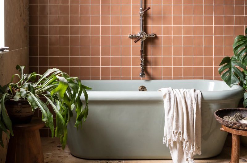 Bathroom design with stone-inspired flooring, a coloured bath, square orange tiles, and house plants.