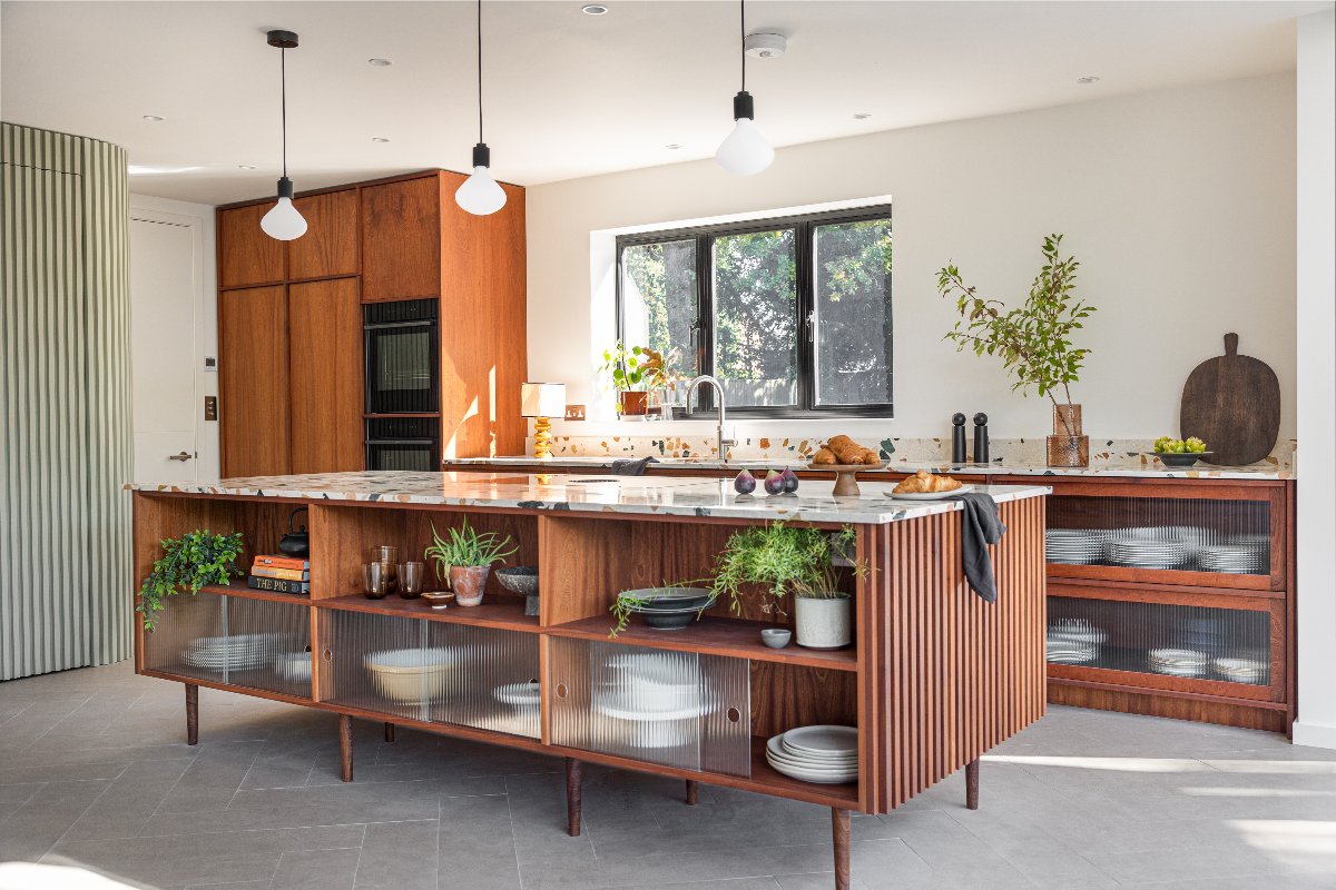 A retro scheme with fluted wood island and cabinetry, terrazzo surfaces, reeded glass cabinets and natural decor.