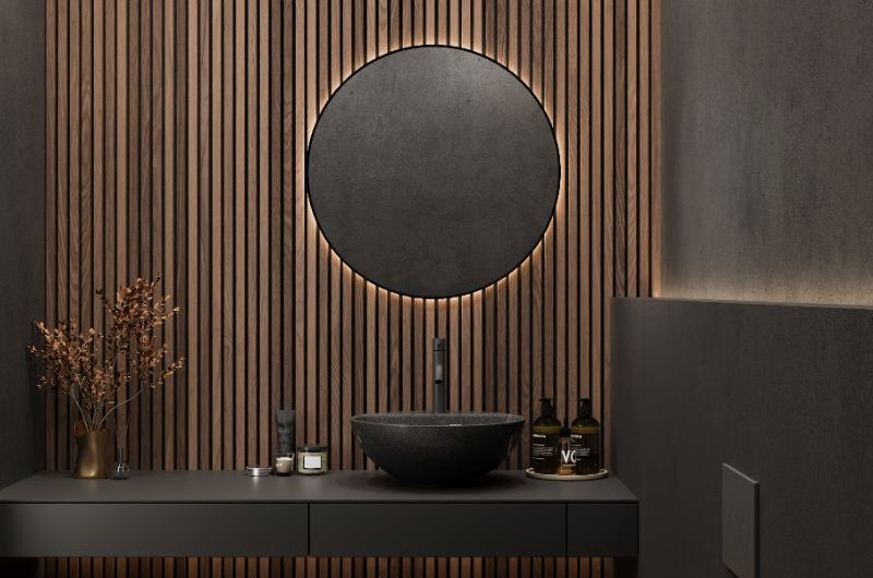 A modern bathroom design with fluted wall panelling, LED mirror, wall-mounted vanity, a countertop basin, and black toilet.