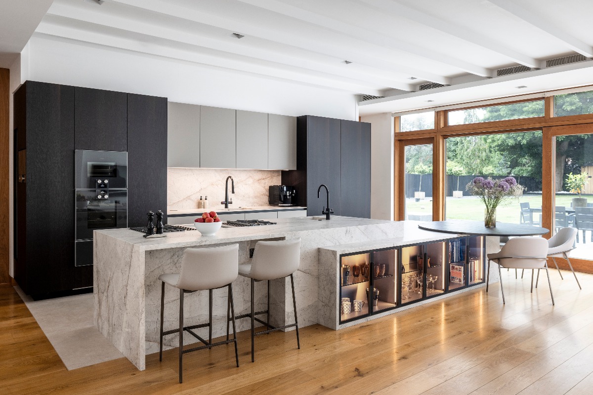 A spacious kitchen with tall cabinets in dark wood and grey, marble surfaces, and glass illuminated cupboards.