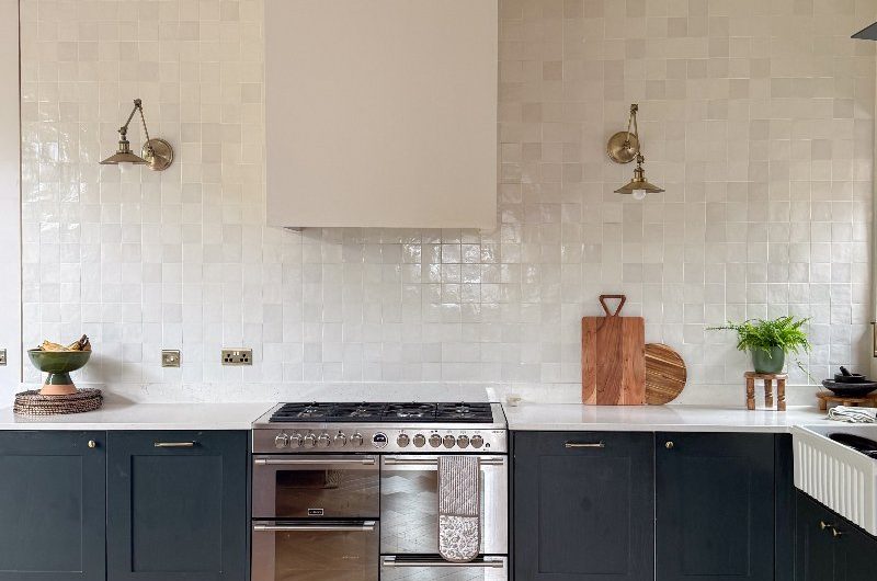 An L-shaped kitchen with a wall clad in zellige tile, dark cabinetry, stainless steel range cooker, and a fluted sink.