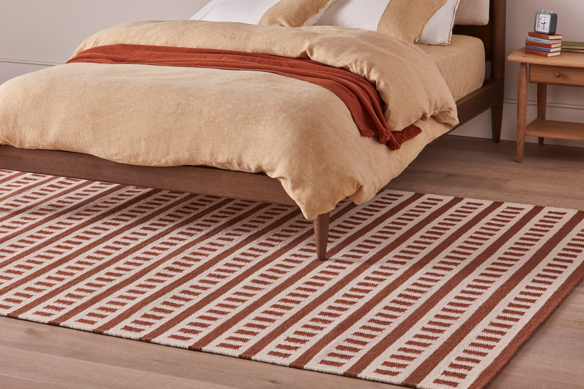 Bedroom design with neutral bedding, a wood frame, wood side table, and striped rug.