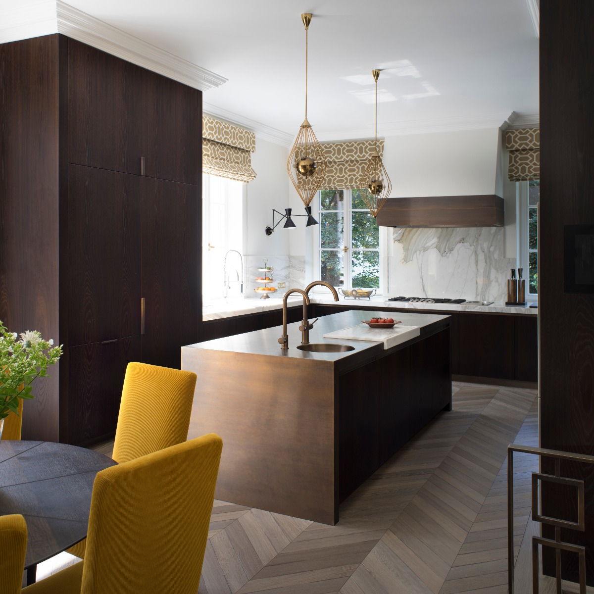 A luxurious scheme with dark wood cabinetry, a central metallic island with a circular sink and two taps, and glamorous pendant lights.