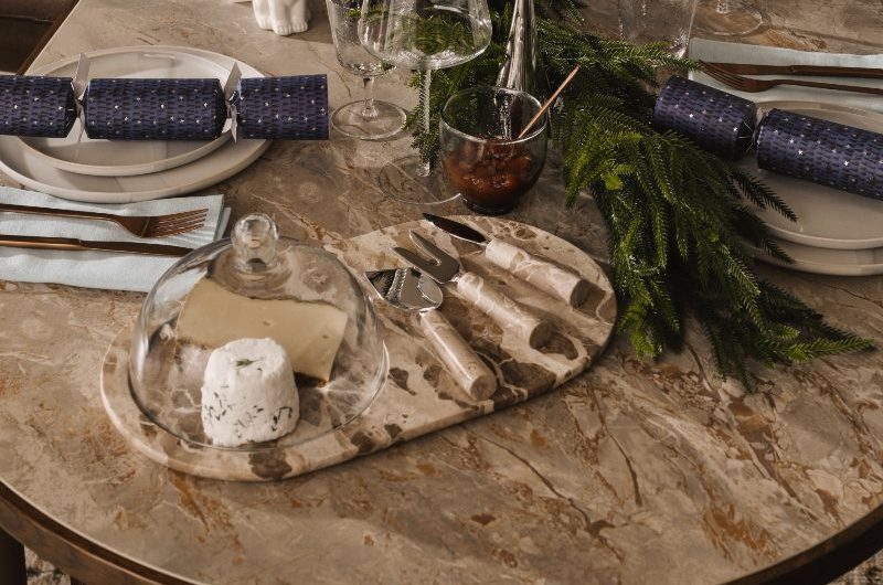 A modern Christmas tablescape with stone cheese board, blue crackers, white plates, and chrome decor.